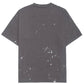 The Domrebel Atelier Pocket Tee Coal Paint by DOM REBEL is a dark gray tee with stylish paint splatter, short sleeves, and a textured cross detail on the upper back.