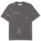 The Domrebel Atelier Pocket Tee Coal Paint by DOM REBEL features "D.R.S.M. ATELIER" text, a chest pocket, signature paint splatter design, and a small label.