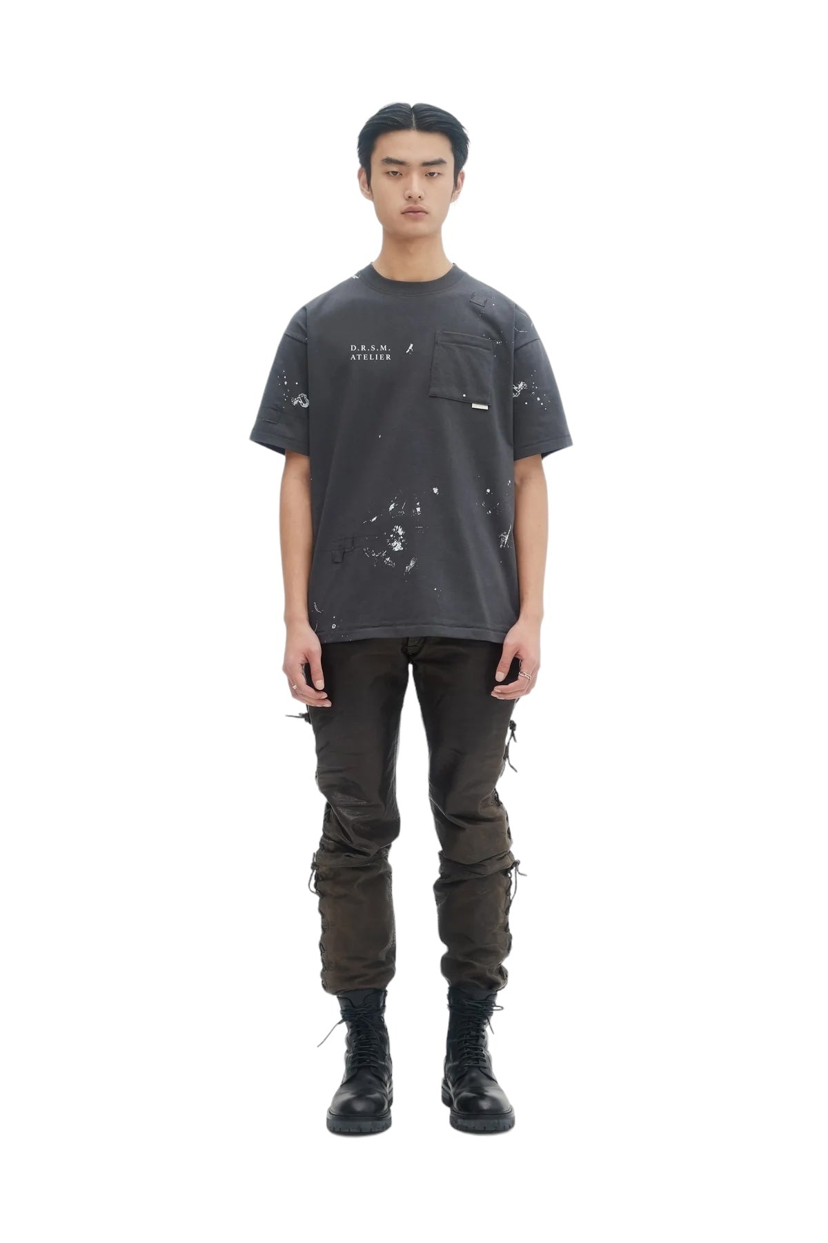 Against a white background, a person wears the DOM REBEL Domrebel Atelier Pocket Tee Coal Paint, paired with cargo pants and black boots.