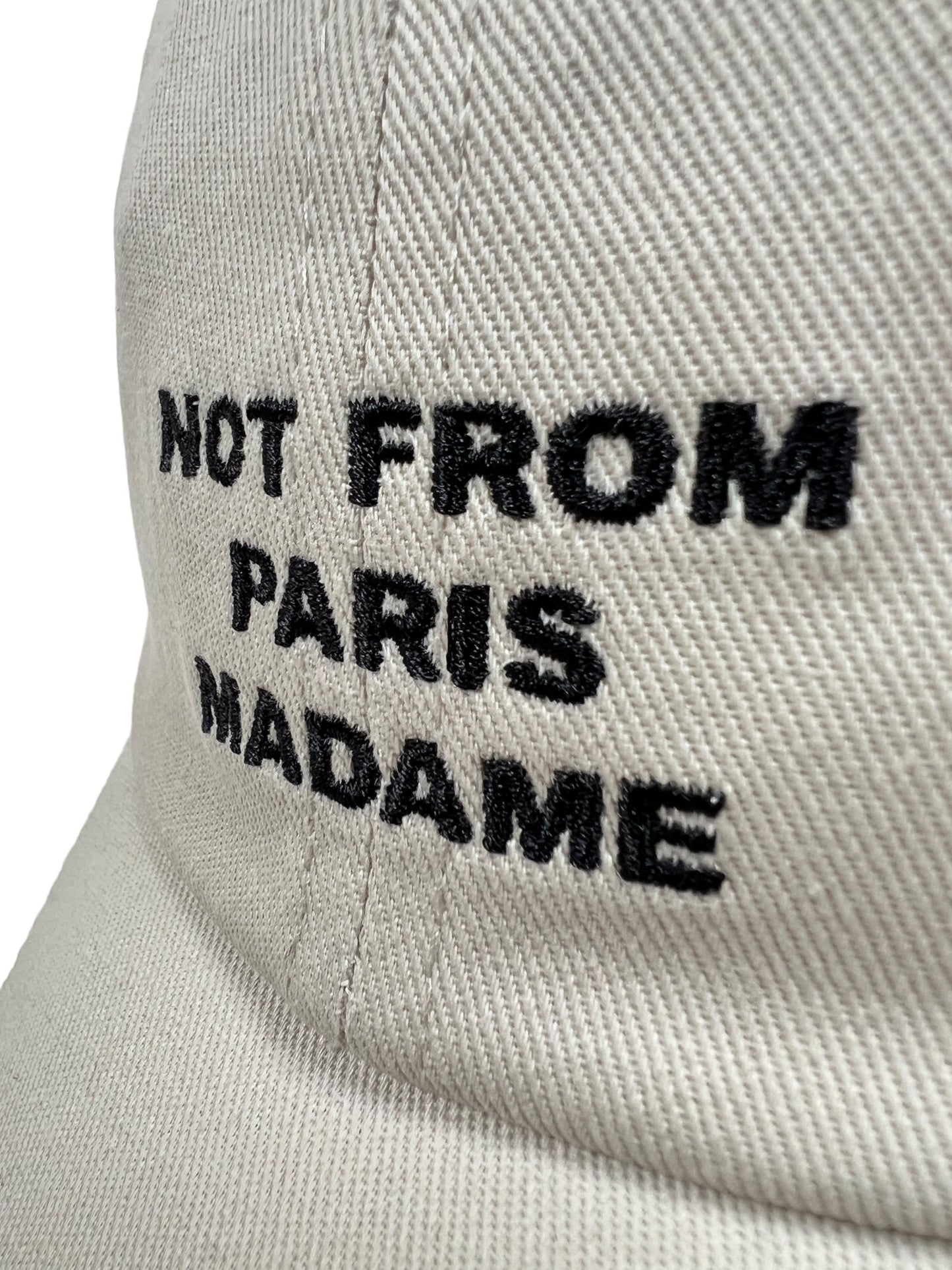 Close-up of the DROLE DE MONSIEUR CP151-CO138-MT LA CASQUETTE SLOGAN MASTIC, a beige cotton baseball hat with "NOT FROM PARIS MADAME" embroidered in black.