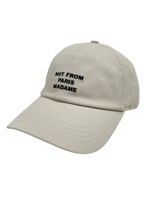 The DROLE DE MONSIEUR CP151-CO138-MT LA CASQUETTE SLOGAN MASTIC, a beige baseball hat made from 100% cotton, features the "NOT FROM PARIS MADAME" slogan embroidered in black on the front.