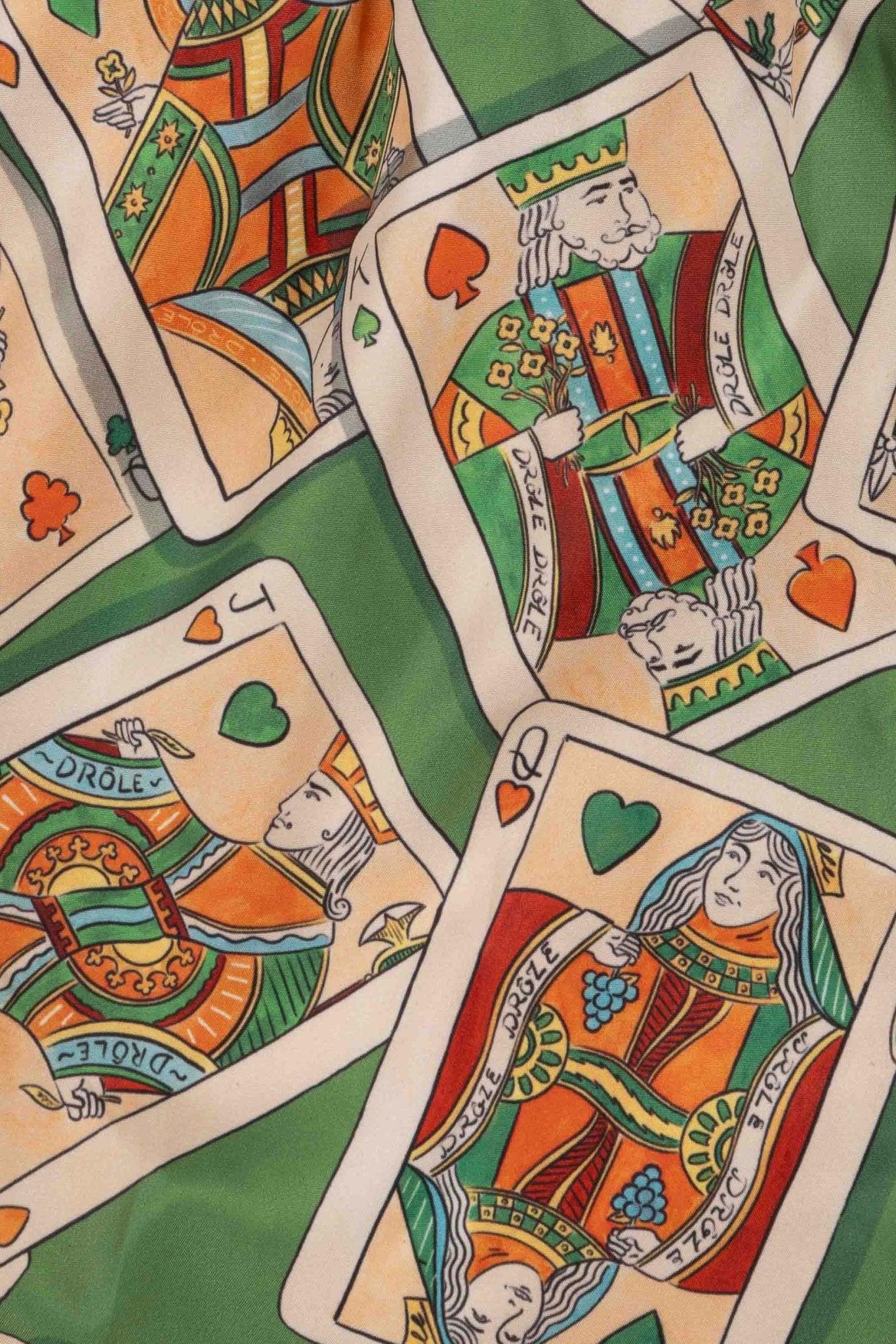 Scattered playing cards with face card designs on a patterned green background, featured in the Drole de Monsieur D-BS141-PL136 Le Short Plage Jeu de Cartes GN swim shorts' card game print with an elastic waist and drawstring.