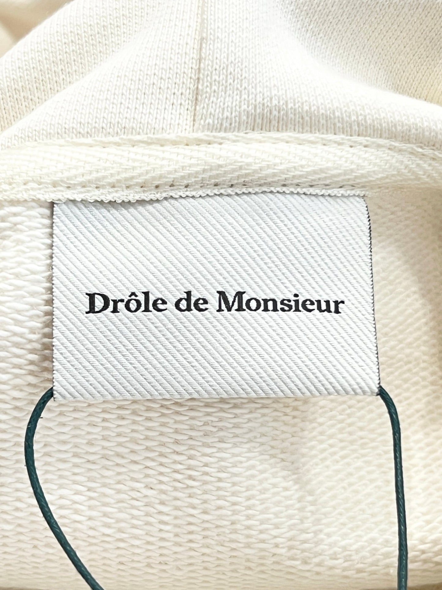 White textile label with the words "DROLE DE MONSIEUR" on a DROLE DE MONSIEUR D-SW144-CO127 LE SWEATSHIRT APRES-MIDI background.