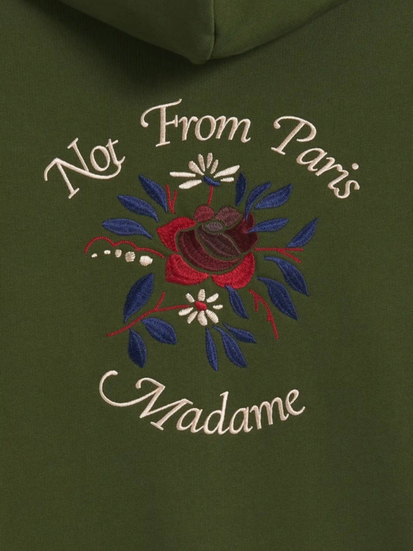 Close-up of the DROLE DE MONSIEUR E-HO169-CO127-KK LE HOODIE FLEURS KAKI in green French terry fabric, featuring embroidered text "Not From Paris Madame" above and below a floral design, resembling a sophisticated slogan fleurs embroidery.