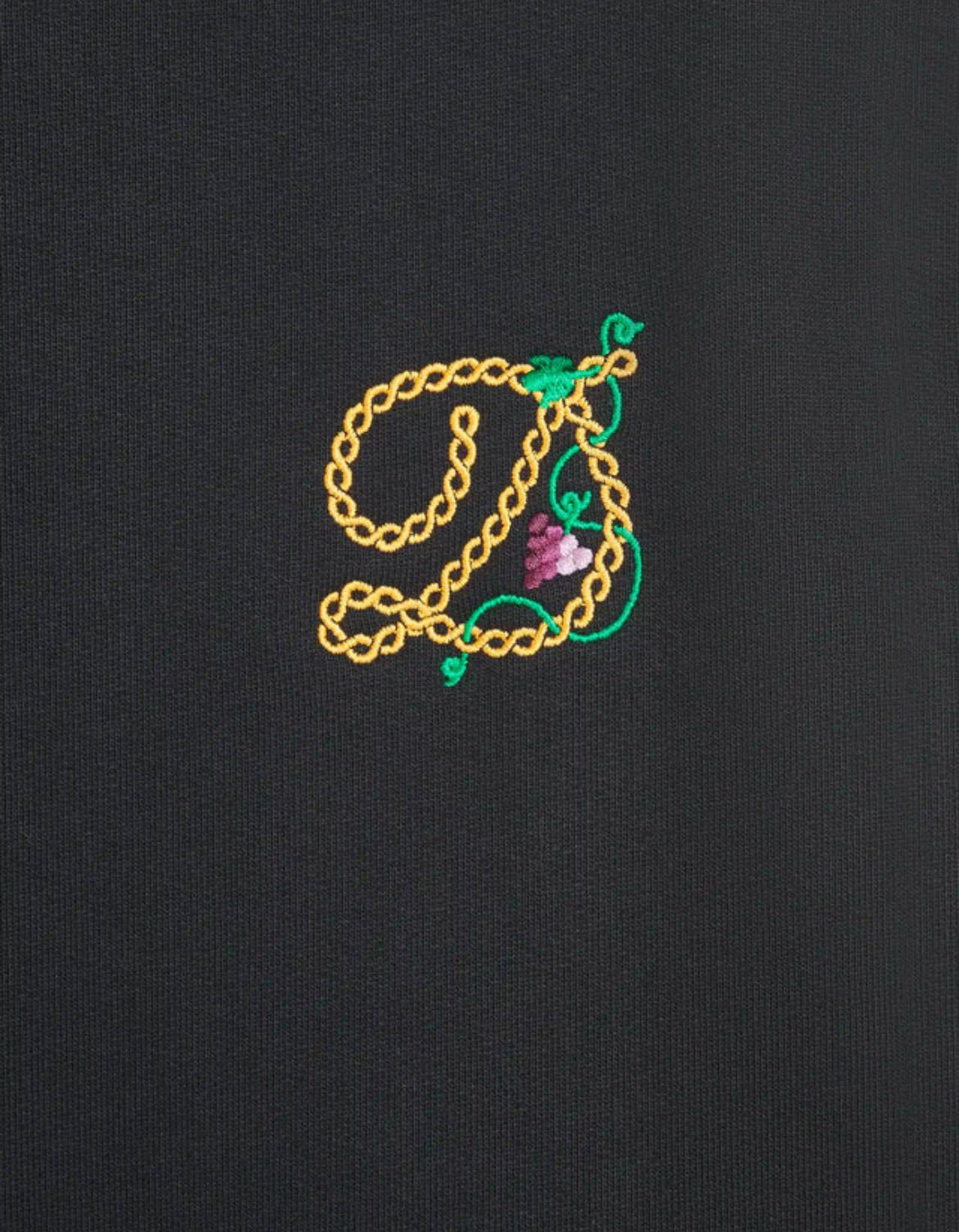 The DROLE DE MONSIEUR E-HO170-CO127-BL LE HOODIE RAISIN BLK features an embroidered letter "E" in yellow thread, adorned with green vines and a small purple cluster of grapes on dark fabric French terry.