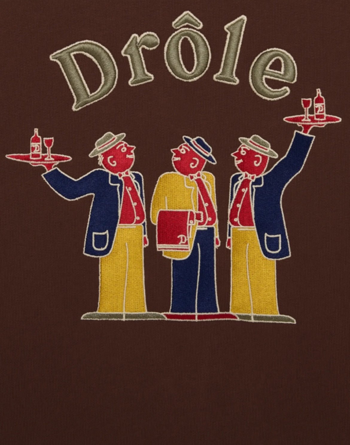 Illustration of three stylized waiters in colorful outfits holding trays with drinks, under the word "DROLE," all expertly rendered on a 100% cotton DROLE DE MONSIEUR E-HO172-CO127-DBN LE HOODIE CRILLON BRW canvas against a dark background.