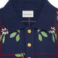 Close-up of the DROLE DE MONSIEUR E-PL135-CO127-NY LE POLO FLEURS NVY, featuring a navy blue fleece fabric with floral patterns, gold buttons, and a ribbed collar. The label reads "Drôle de Monsieur".
