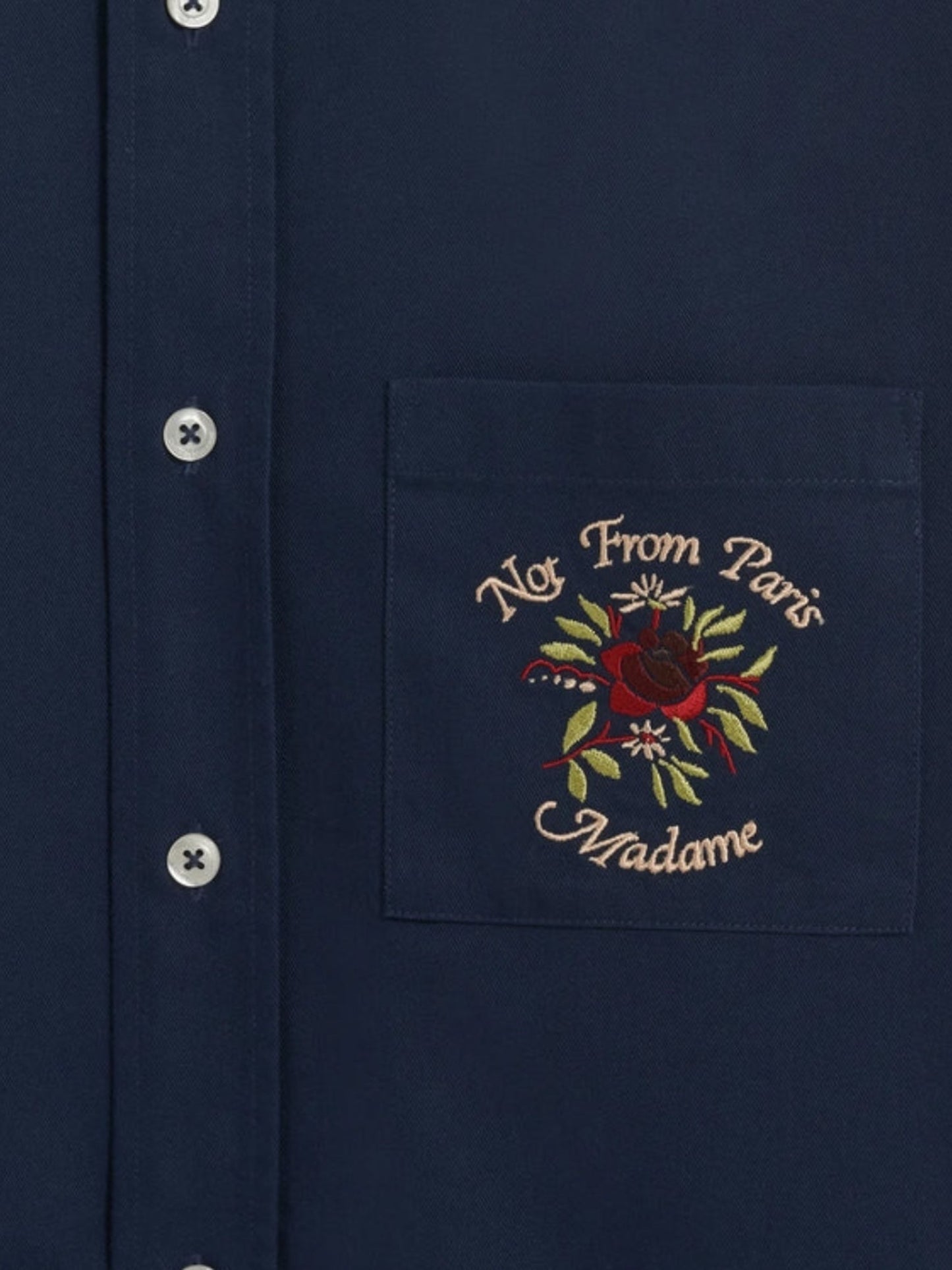 Close-up of the DROLE DE MONSIEUR E-SH189-PL149-NY LA CHEMISE NAVY, a navy long-sleeved shirt with white buttons and a chest patch pocket. The pocket features slogan embroidery with the text "Not From Paris Madame" and a red rose design.