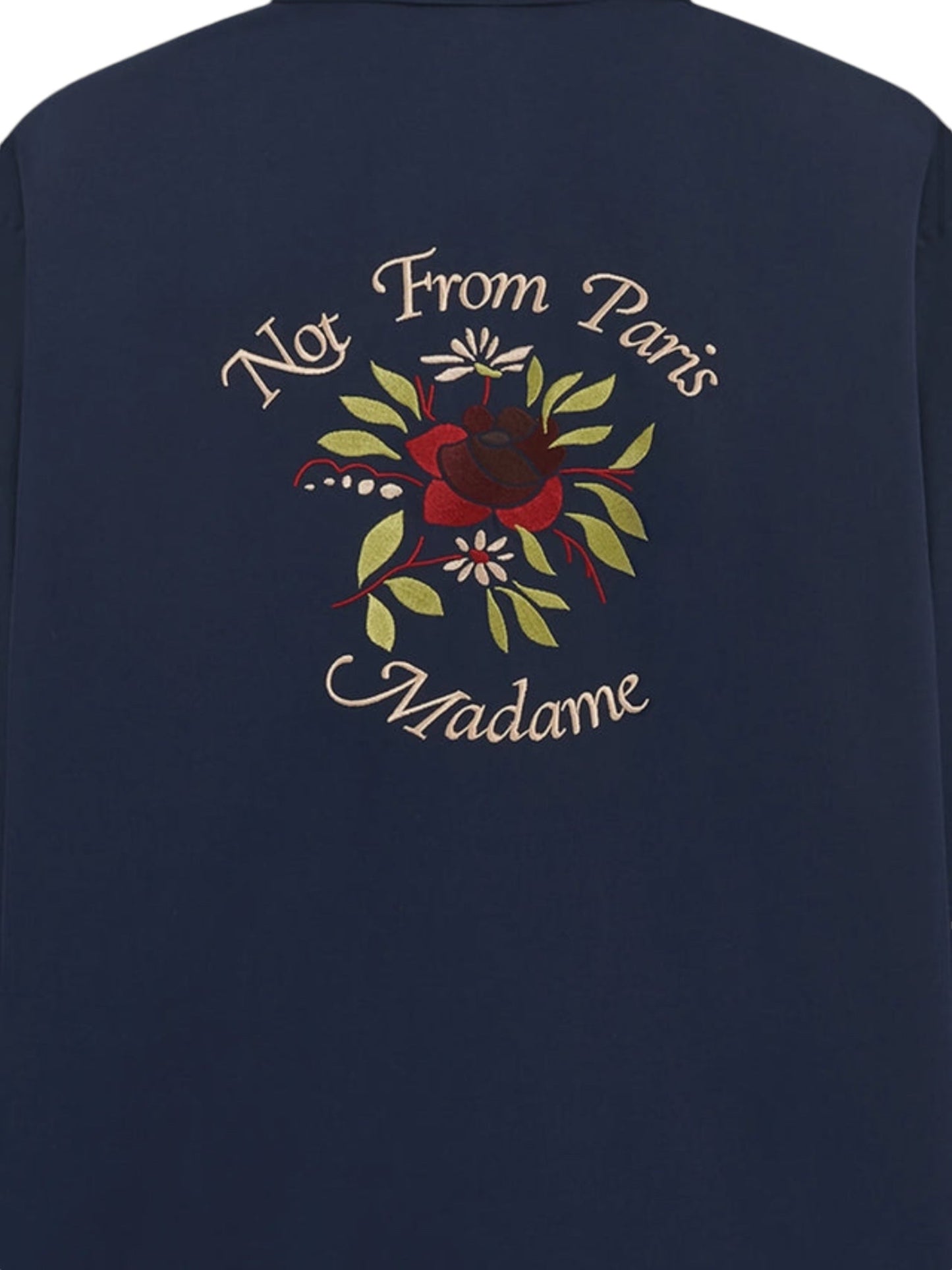 Introducing the DROLE DE MONSIEUR E-SH189-PL149-NY LA CHEMISE NAVY, a navy long-sleeved shirt adorned with intricate floral embroidery and a convenient chest patch pocket. The back of the shirt elegantly showcases the slogan "Not From Paris Madame," embodying its unique charm.