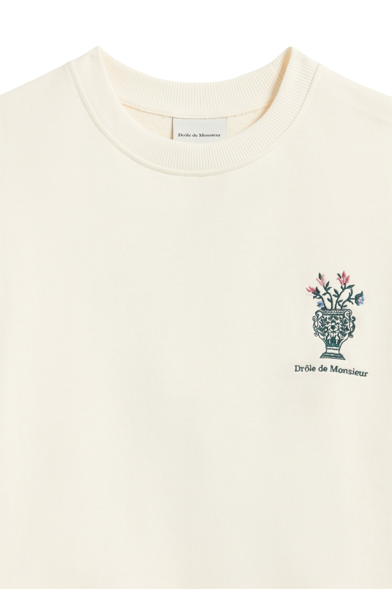 A cream-colored French terry sweatshirt by DROLE DE MONSIEUR, featuring a small floral vase embroidery and the text "Drôle de Monsieur" printed on the left chest area. Model: E-SW153-CO127-CM LE SWEATSHIRT CREAM.