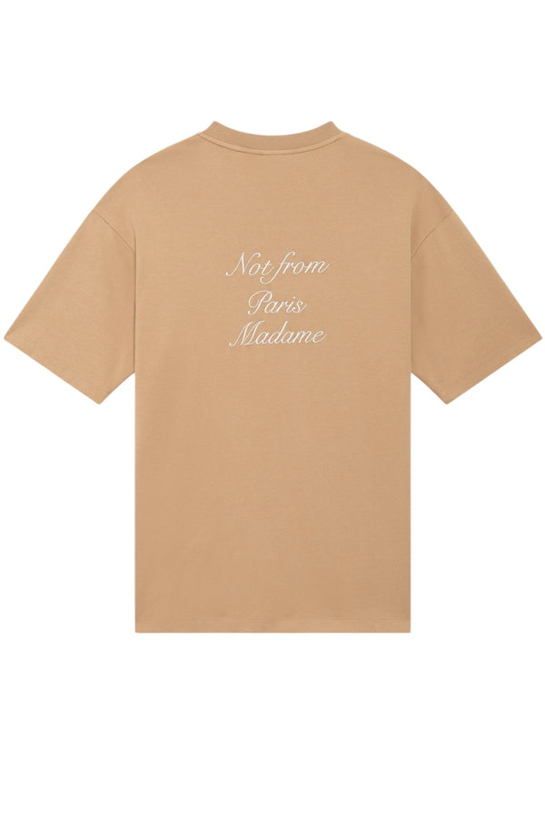 Beige cotton t-shirt, model E-TS209-CO002-IBN LE T-SHIRT BRW by DROLE DE MONSIEUR, featuring short sleeves and a crew neck. Made from soft interlock fabric with the phrase "Not From Paris Madame" elegantly printed in white on the left chest area.