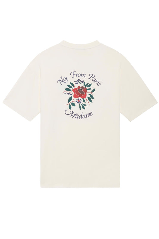 A white cotton T-shirt from DROLE DE MONSIEUR, model E-TS210-CO002-CM Le T-Shirt Cream, with a ribbed neckline and a design on the back featuring a red flower and green leaves, accompanied by the slogan "Not From Paris Madame.