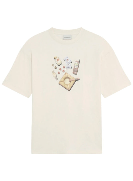 A collection of items including perfume, playing cards, a mobile phone, dice, a watch, rings, and an ashtray with a cigar on a plain background. Amongst these is the DROLE DE MONSIEUR E-TS218-CO002-CM LE T-SHIRT SOIREE CREAM featuring an elegant Soirée print.