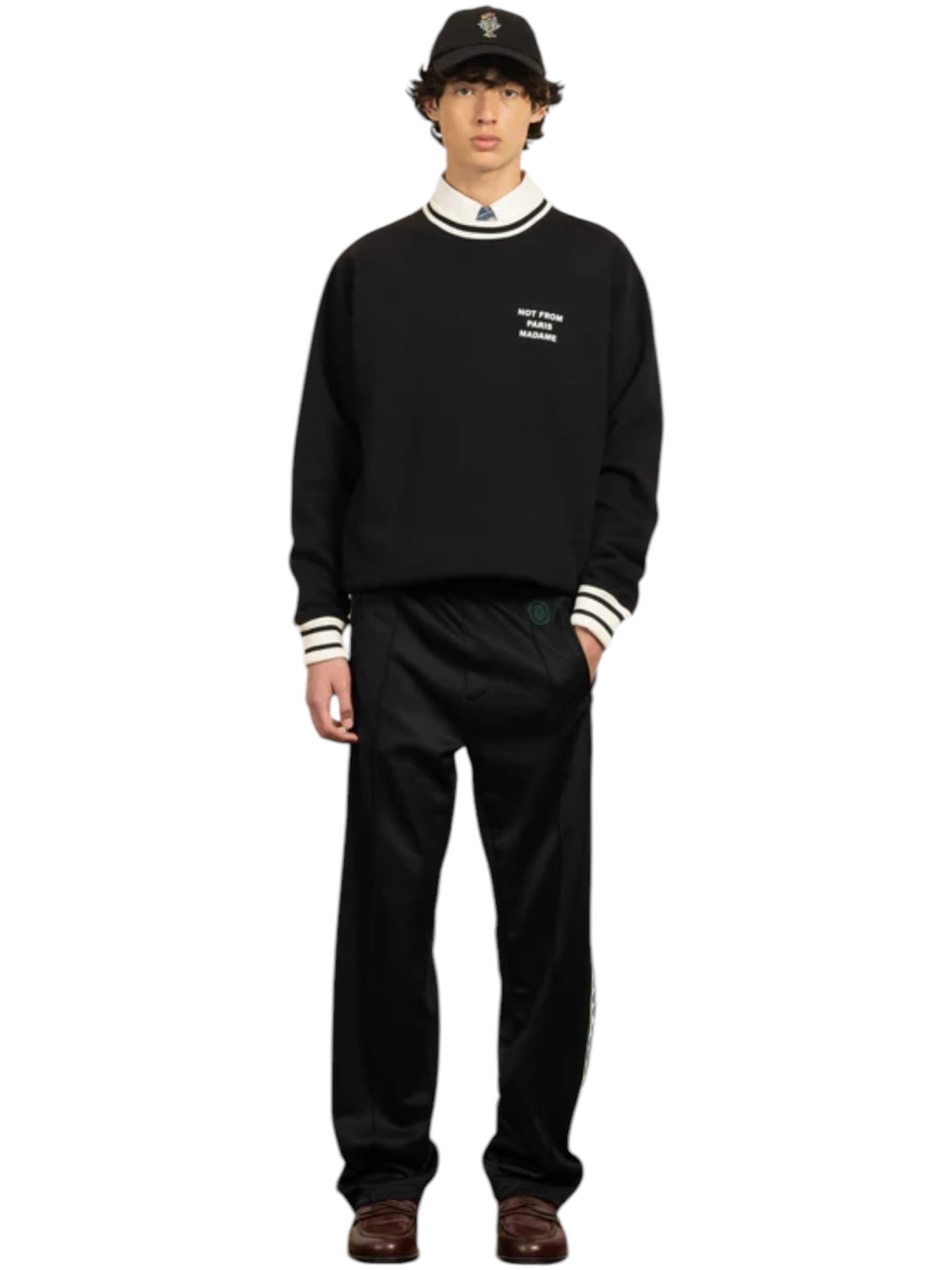 A person stands against a white background in the Drôle de Monsieur F-SW140-CO127-Bl Le Sweatshirt Black, a classic 100% cotton French terry piece, with matching pants, a white collared shirt, and brown shoes.