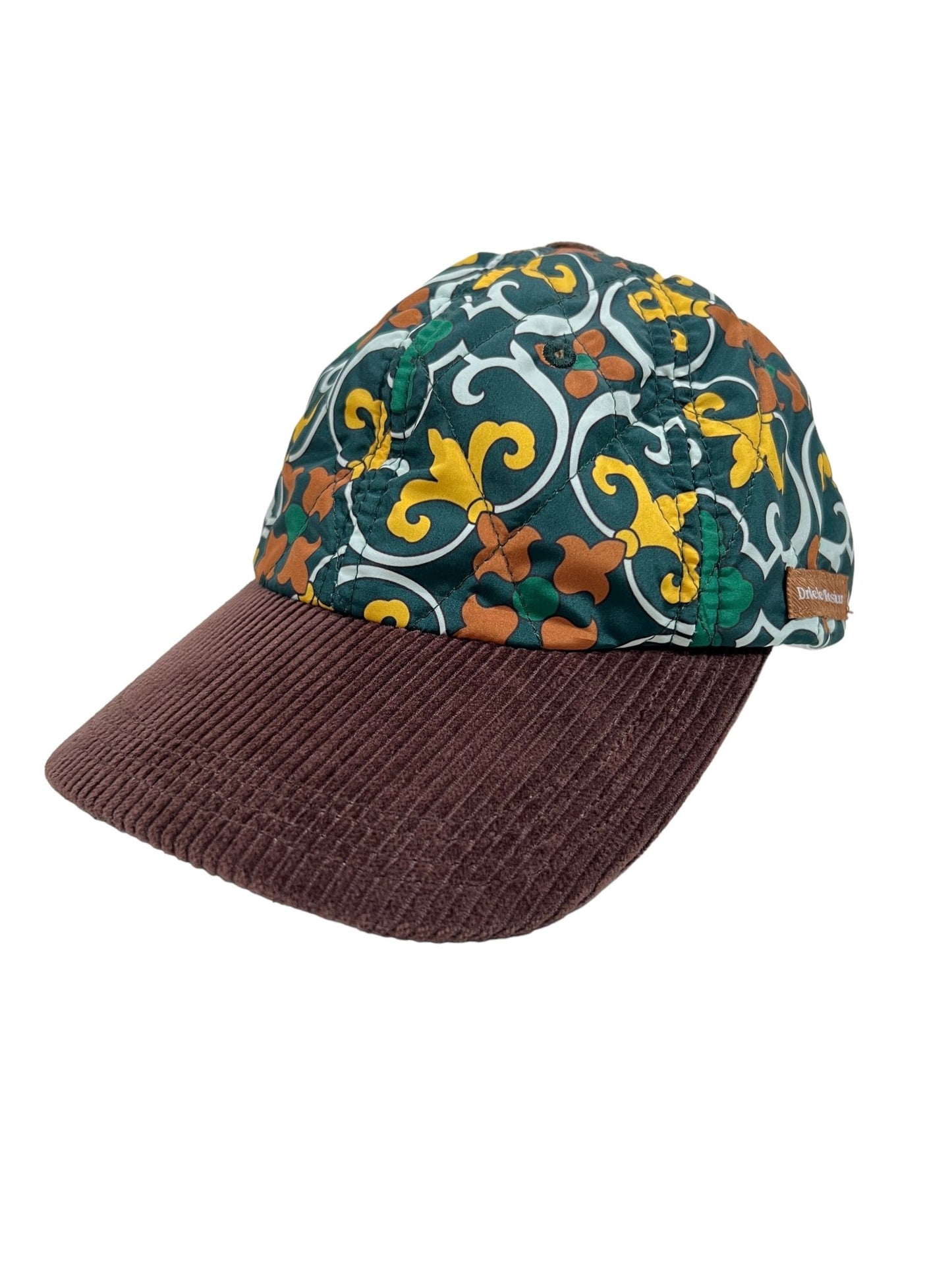 The DROLE DE MONSIEUR HAT B-CP123 LA CASQUETTE FAIENCE GREEN features a brown corduroy brim paired with a top adorned in a vibrant digital print of green, yellow, and orange florals.