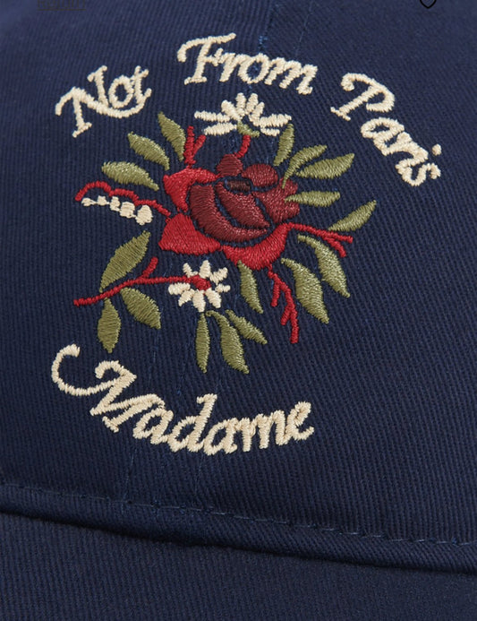 A close-up of the DROLE DE MONSIEUR I E-CP153-CO138-DNY LA CASQUETTE NVY hat in navy blue showcases the text "Not From Paris Madame" embroidered above an ornate floral design.