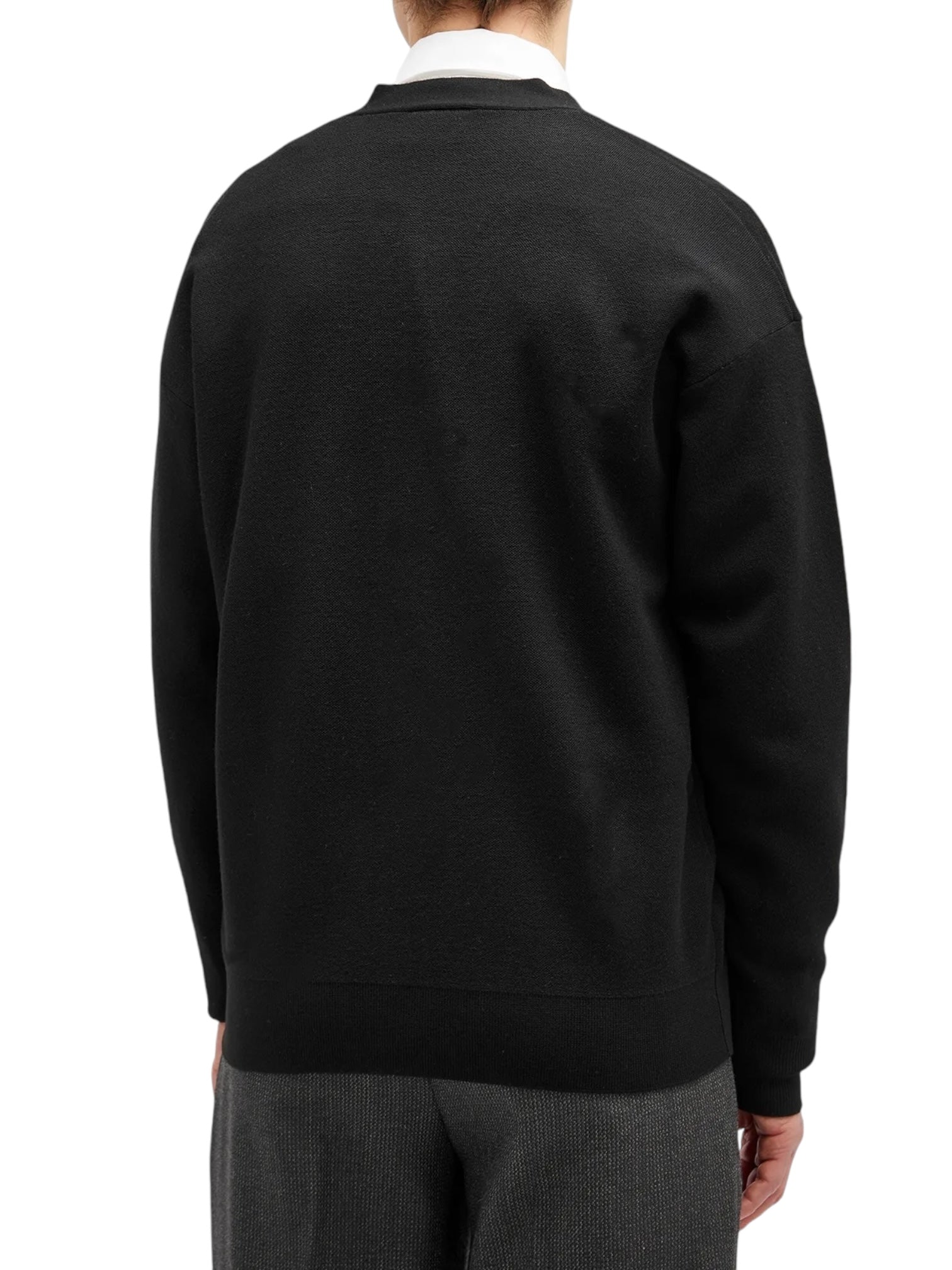 A person is seen from the back, wearing a Drôle de Monsieur black cardigan over a white collared shirt and gray pants, against a plain white background.