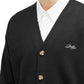 Someone is wearing the Drôle de Monsieur Perm-CA123-WO007-BL LE Cardigan Blk, a black wool cardigan with ribbed trim and buttons, layered over a white collared shirt. It features a small Drôle embroidery logo on the left side.