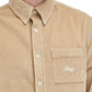 A person wearing the Drôle de Monsieur La Chemise Beige, featuring a corduroy button-up design with embroidery on the pocket and long sleeves.