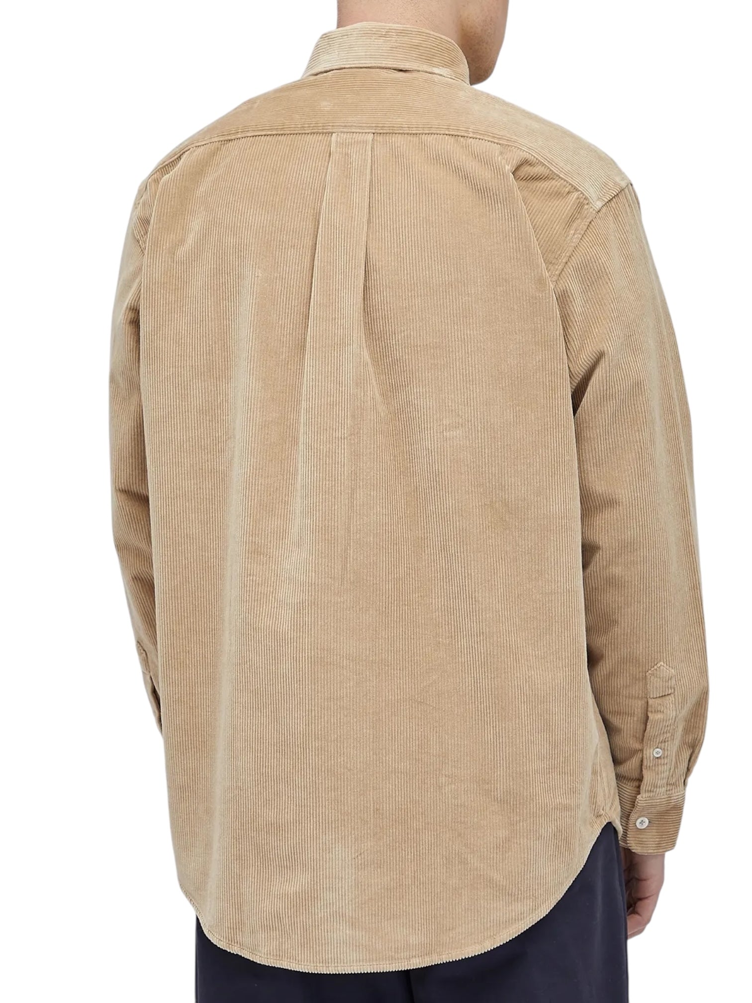 Viewed from the back, a person wears the Drôle de Monsieur Perm-SH172-CO156-BG La Chemise Beige shirt. This corduroy piece has long sleeves with buttoned cuffs and features distinctive Drôle embroidery, adding elegance to its design.