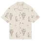 The Drôle de Monsieur SH214-CO198-EC La Chemise Brodee Ecru is a beige short-sleeved cotton blend shirt with outlined dogs, potted plants, cocktail glasses, and cherries for a playful yet refined look.