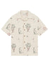 The Drôle de Monsieur SH214-CO198-EC La Chemise Brodee Ecru is a beige short-sleeved cotton blend shirt with outlined dogs, potted plants, cocktail glasses, and cherries for a playful yet refined look.