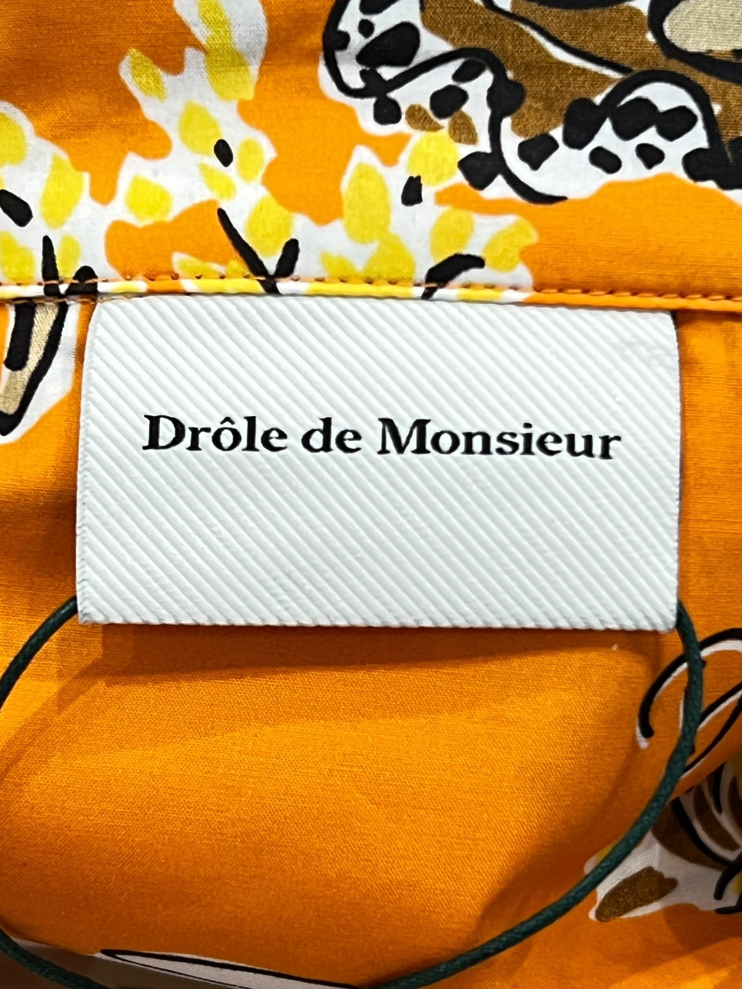 A close-up of a DROLE DE MONSIEUR SHIRT D-SH170-CO128 LA CHEMISE TERRASSE OR on a textured orange short sleeve shirt with a leopard print pattern.