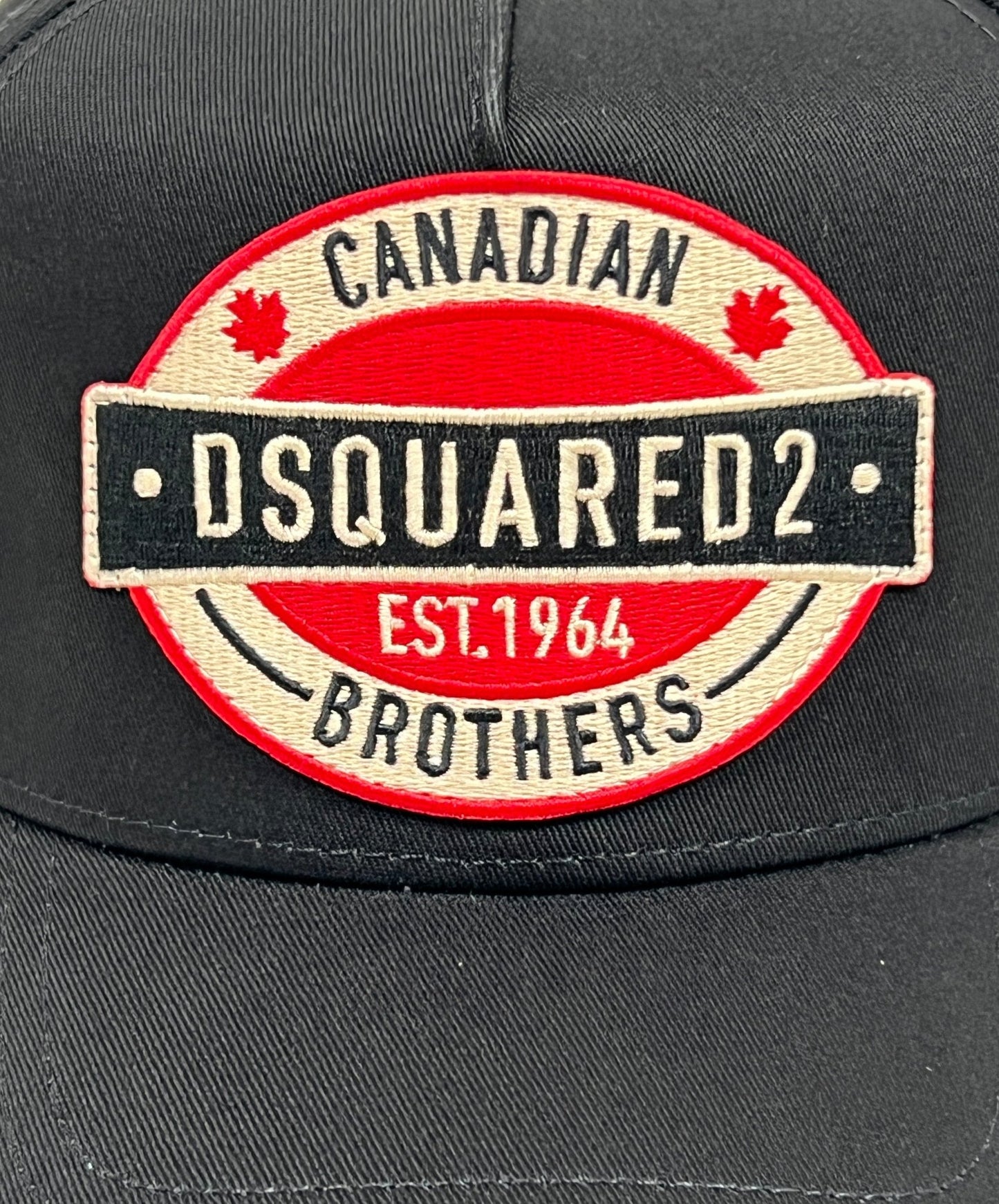 The DSQUARED2 BCM0621 Logo Baseball Cap Col.2124 features a black cotton design adorned with a red and white embroidered patch that reads "Canadian Brothers DSQUARED2 EST. 1964" and includes two small red maple leaves. This stylish cap also comes with an adjustable strap for a perfect fit, offering both fashion and functionality from the renowned brand, DSQUARED2.