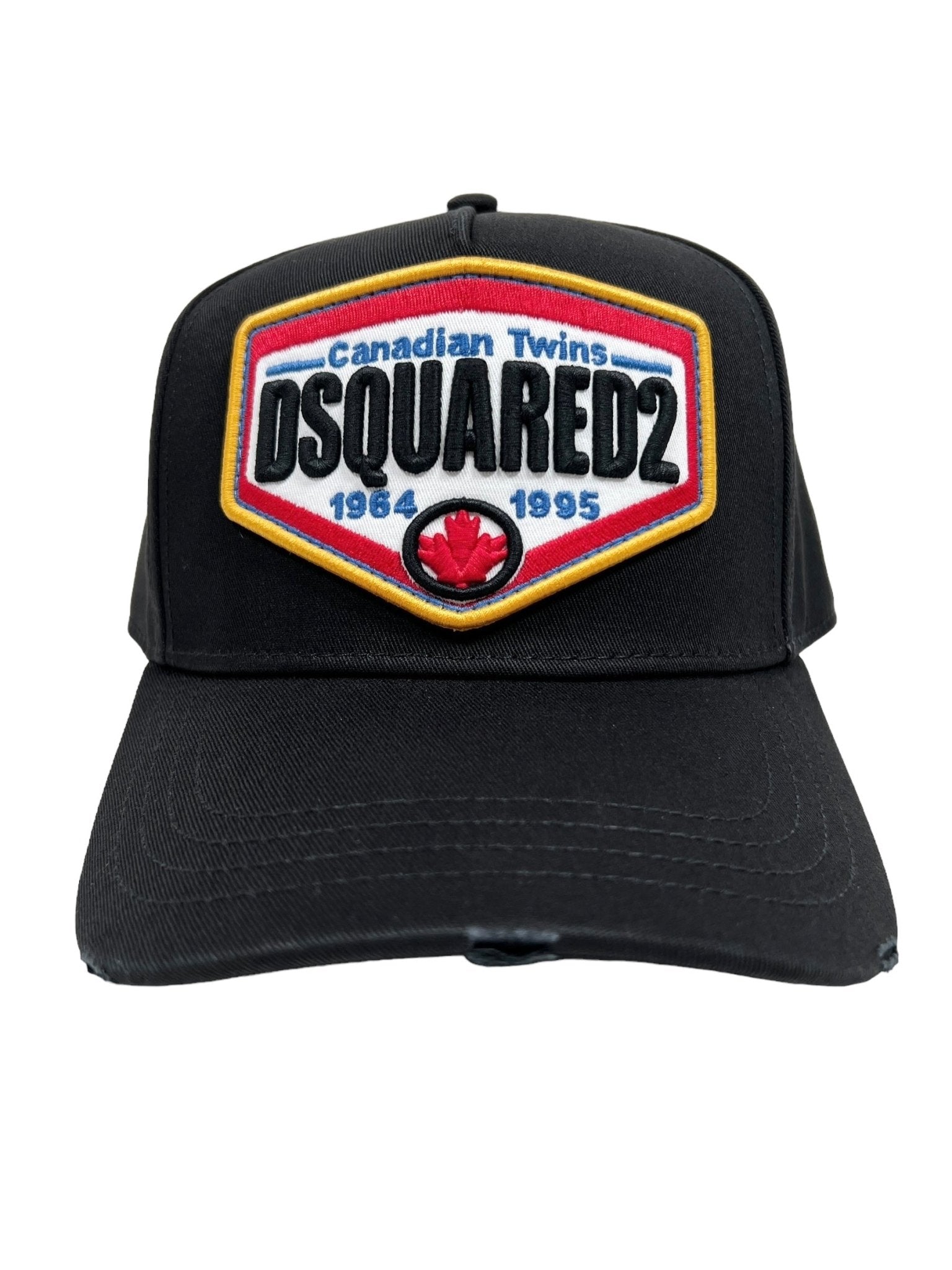 The DSQUARED2 BCM0763 Logo Baseball Cap in black is a stylish accessory featuring a vibrant embroidered patch on the front that reads "Canadian Twins, DSQUARED2, 1964 - 1995" along with a red maple leaf logo. The cap is designed with an adjustable strap to ensure a perfect fit.