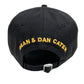 The image shows the back view of a DSQUARED2 BCM0763 LOGO BASEBALL CAP COL.2124 in black, featuring an adjustable strap. The text "DEAN & DAN CATEN" is embroidered in yellow, highlighting its connection to the DSQUARED2 brand.