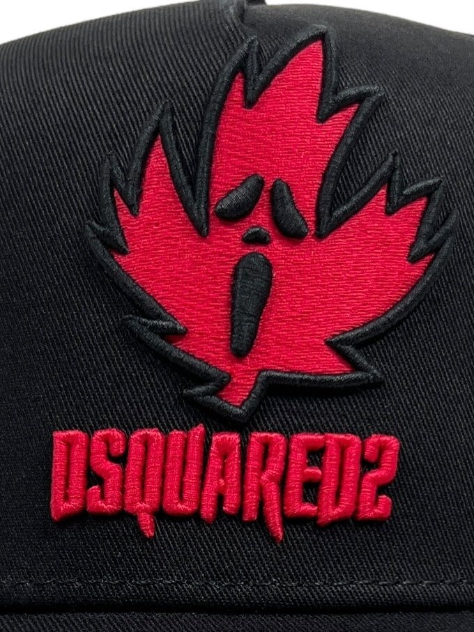 Close-up of the DSQUARED2 BCM0824 Horror Baseball Cap Col.2124 in black, showcasing a red embroidered maple leaf with a face and the text "DSQUARED2" below it, blending sporty aesthetics with urban vibe.