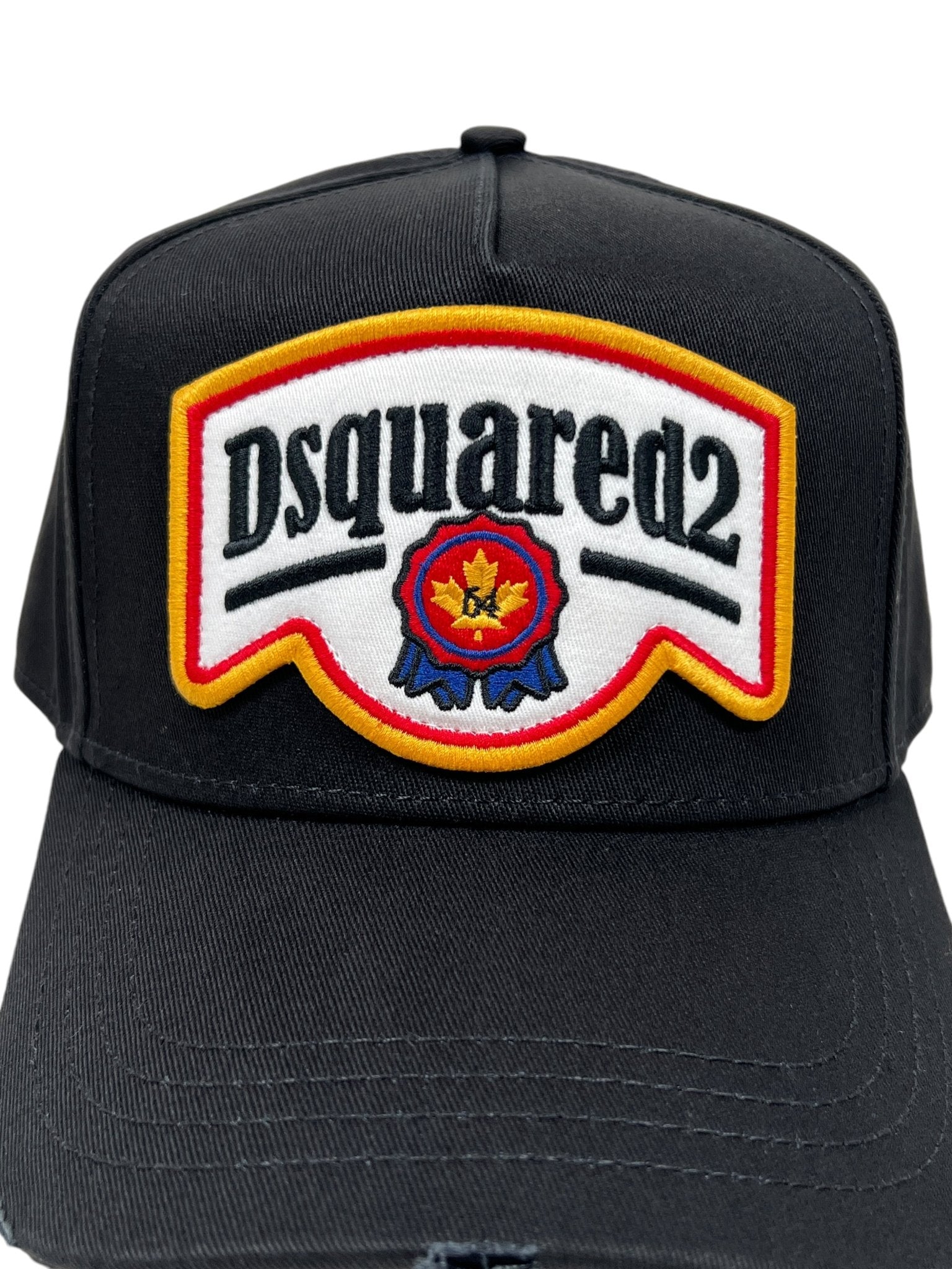 The Dsquared2 BCM0847 Logo Cap in Nero from DSQUARED2 is made of cotton gabardine, showcasing a vibrant red, white, and yellow patch with star and ribbon designs, along with distressed details for an edgy look.