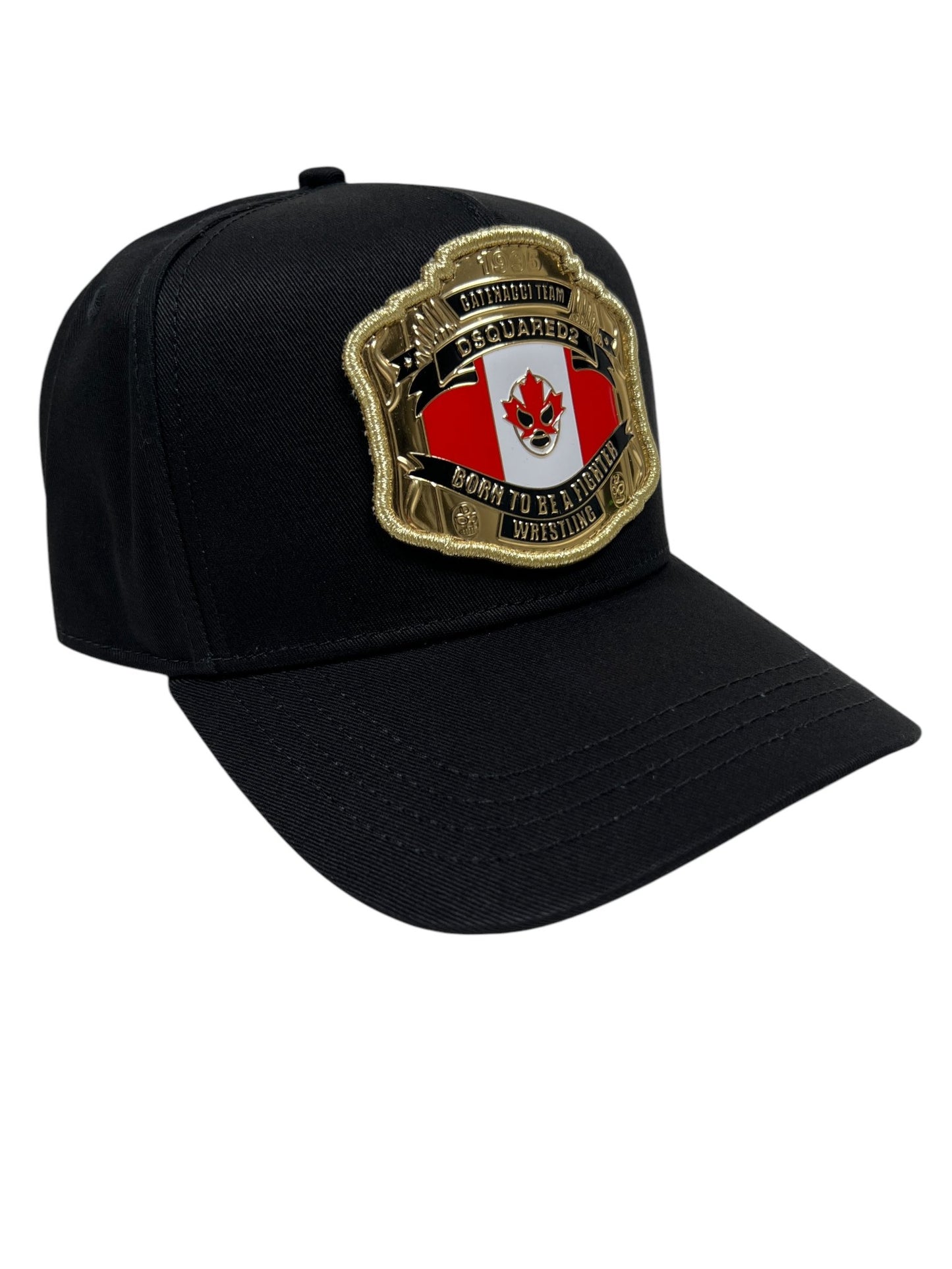 The DSQUARED2 BCM0903 baseball cap in gabardine-nero is a stylish accessory featuring a gold and red embroidered patch that reads "Born to be a professional wrestler" in English and Spanish, with a maple leaf and skull design at the center.