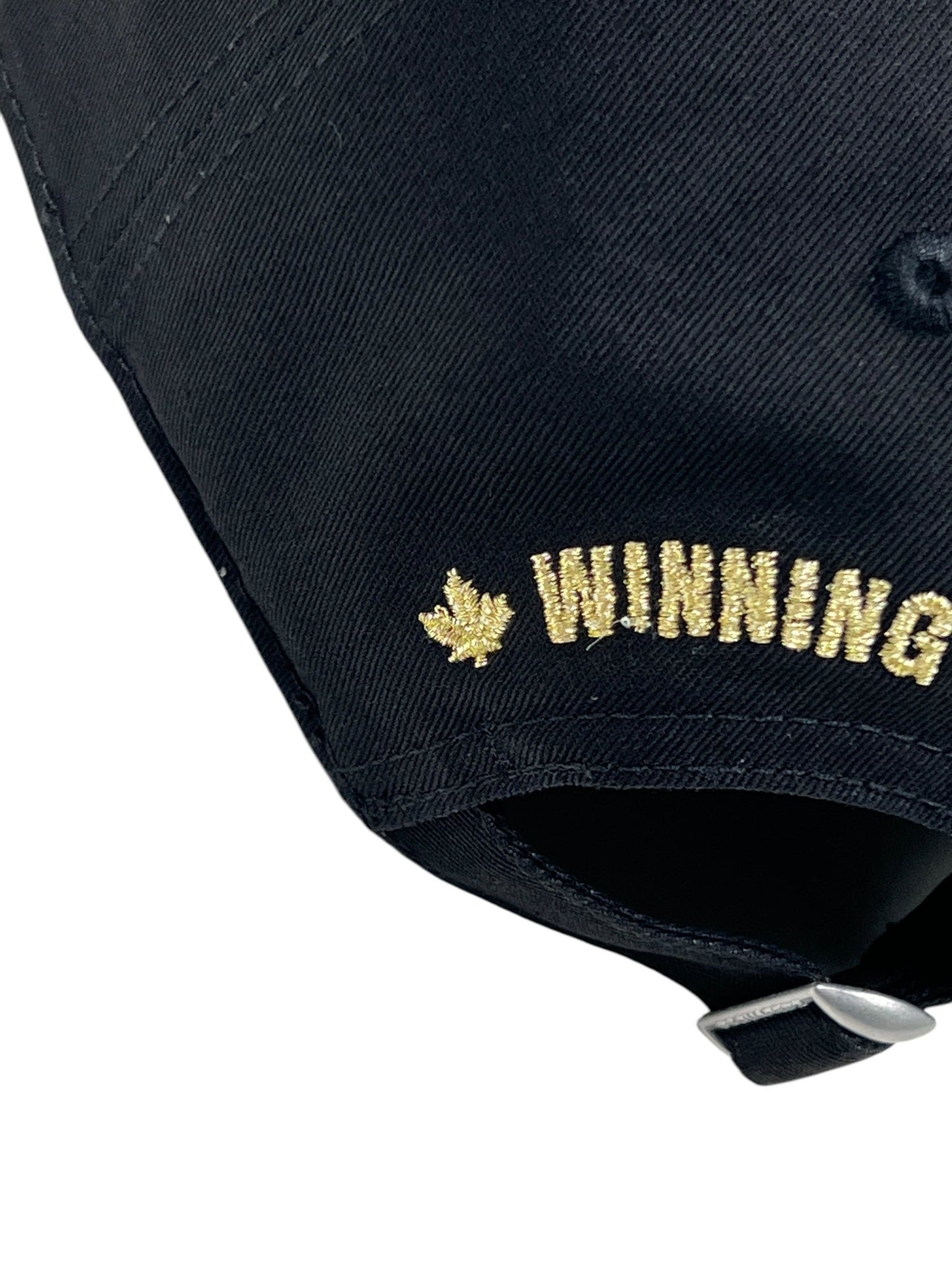 Close-up of a Dsquared2 BCM0903 Baseball Cap Gabardine-Nero, made from cotton gabardine, with "WINNING" embroidered in gold and a leaf design; a stylish DSQUARED2 accessory.