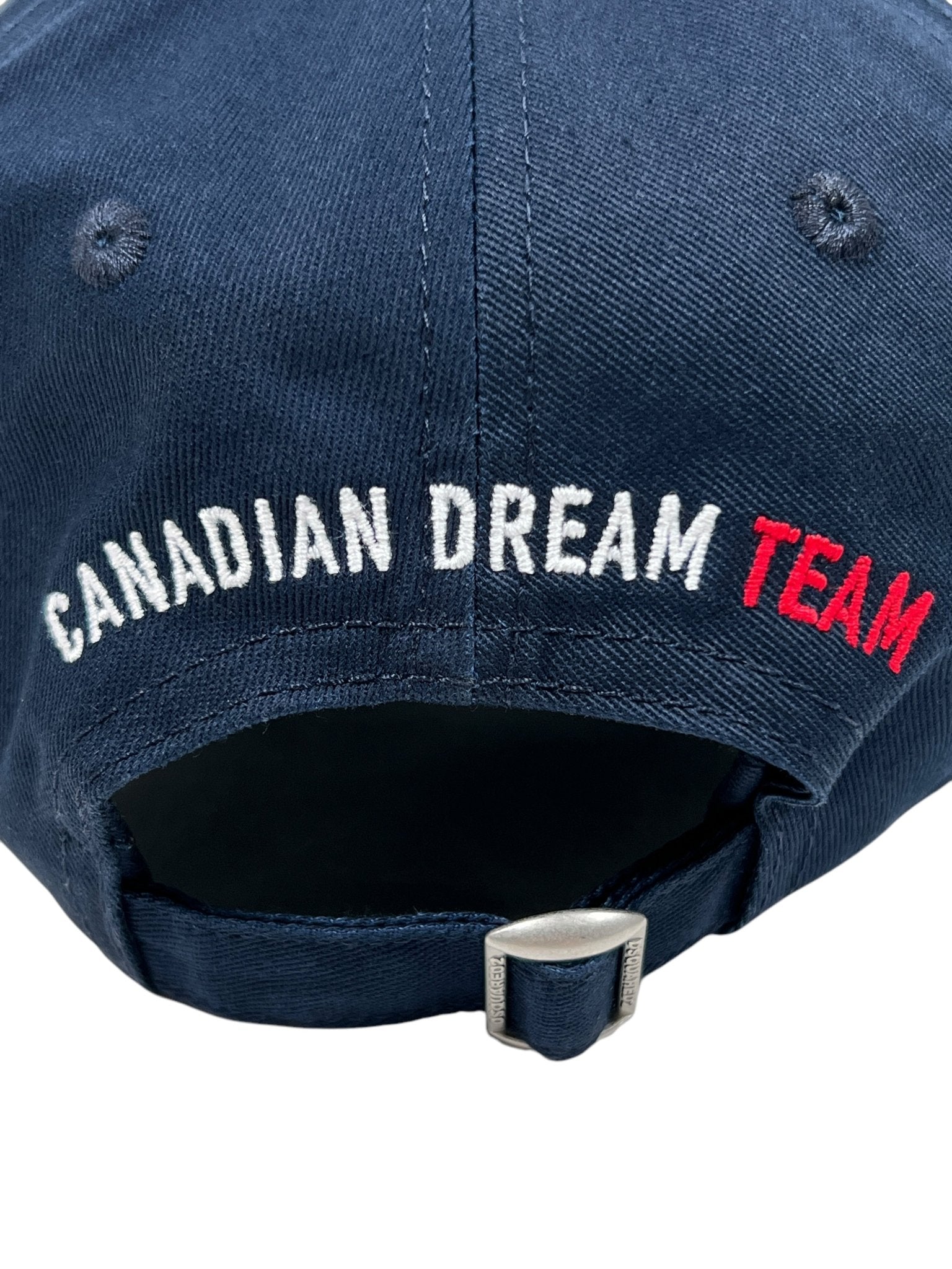 Close-up of a navy Dsquared2 BCM0917 gabardine baseball cap featuring "Canadian Dream Team" embroidered on the back in white and red. This DSQUARED2 hat has an adjustable buckle strap for a perfect fit.
