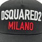 The DSQUARED2 BCM0917 Baseball Cap Gabardine-Nero features "DSQUARED2" in white and "MILANO" in red, offering an adjustable fit for ultimate comfort.