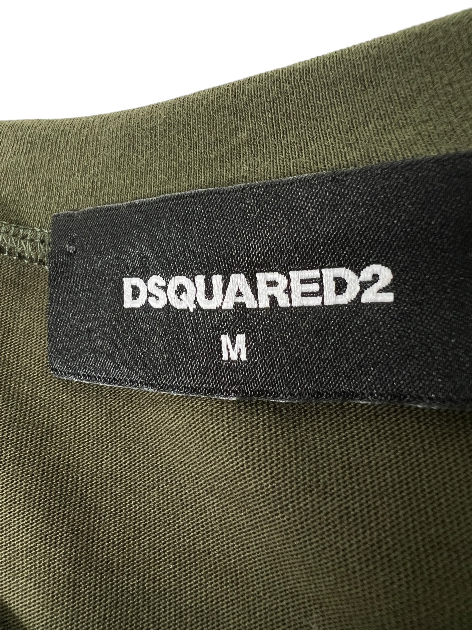 Close-up of a black label with "DSQUARED2" and "M" in white, expertly stitched onto olive fabric, showcasing the iconic style of the Dsquared2 S71Gd1462 Cool Fit Tee Green.