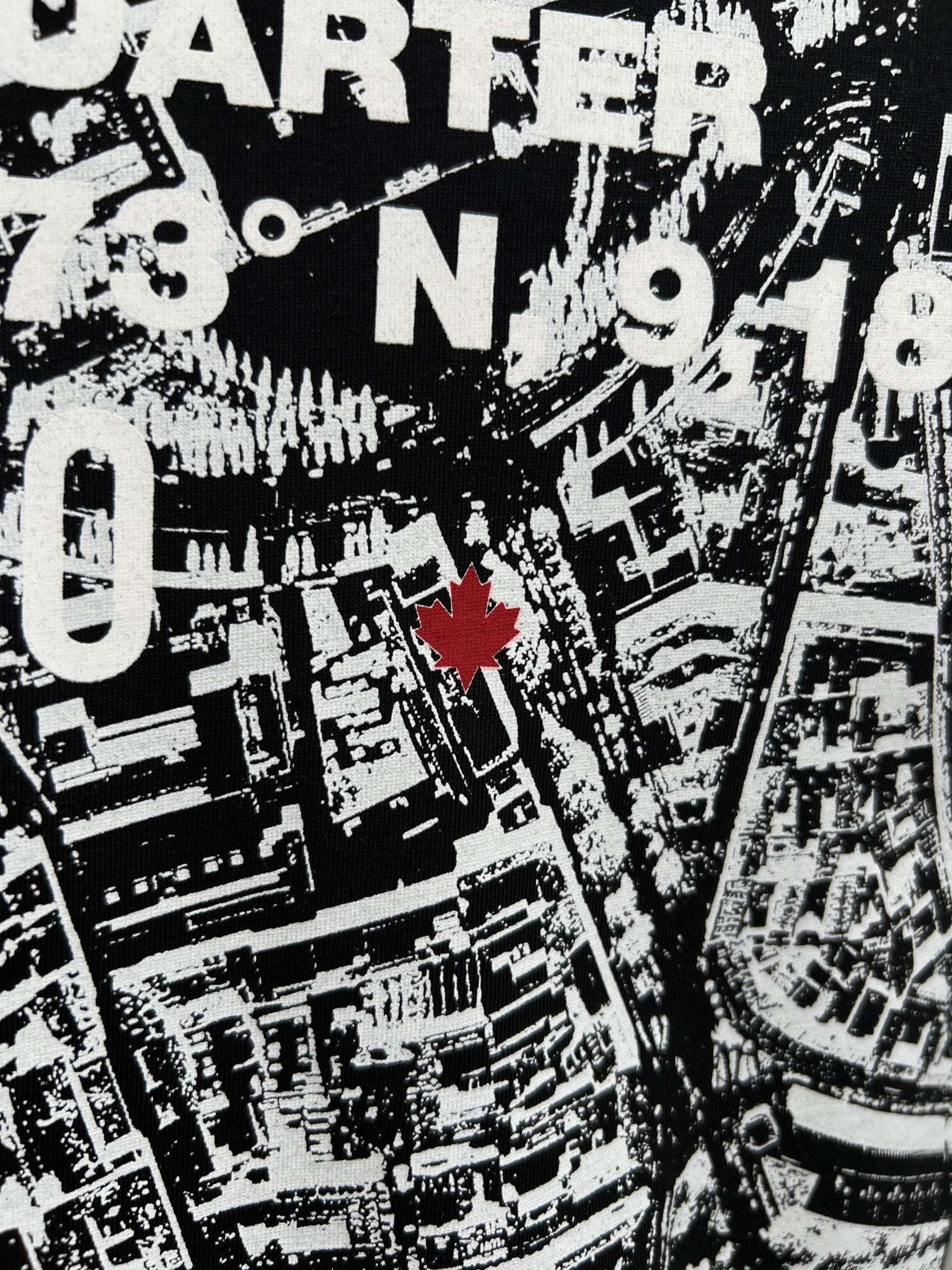 The Dsquared2 S74Gd1338 Cool Fit Tee Black by DSQUARED2 showcases a chic black and white map-inspired design, highlighted with a red maple leaf at its center, and adorned with numbers and text at the top. Crafted from 100% cotton, this T-shirt combines comfort with a striking style statement.