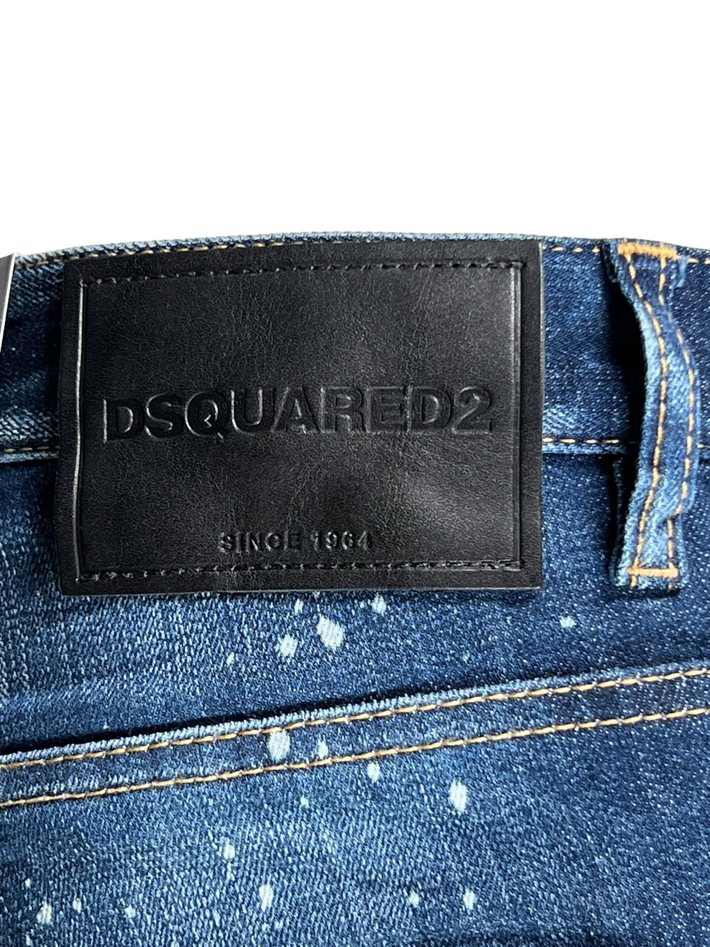 Close-up of a DSQUARED2 denim waistband with a black leather patch that reads "DSQUARED2 SINCE 1964." The trendy ripped detailing and distressed, paint-splatter design highlight the stylish slim fit of these DSQUARED2 S74LB1556 Skater Jeans Navy Blue.