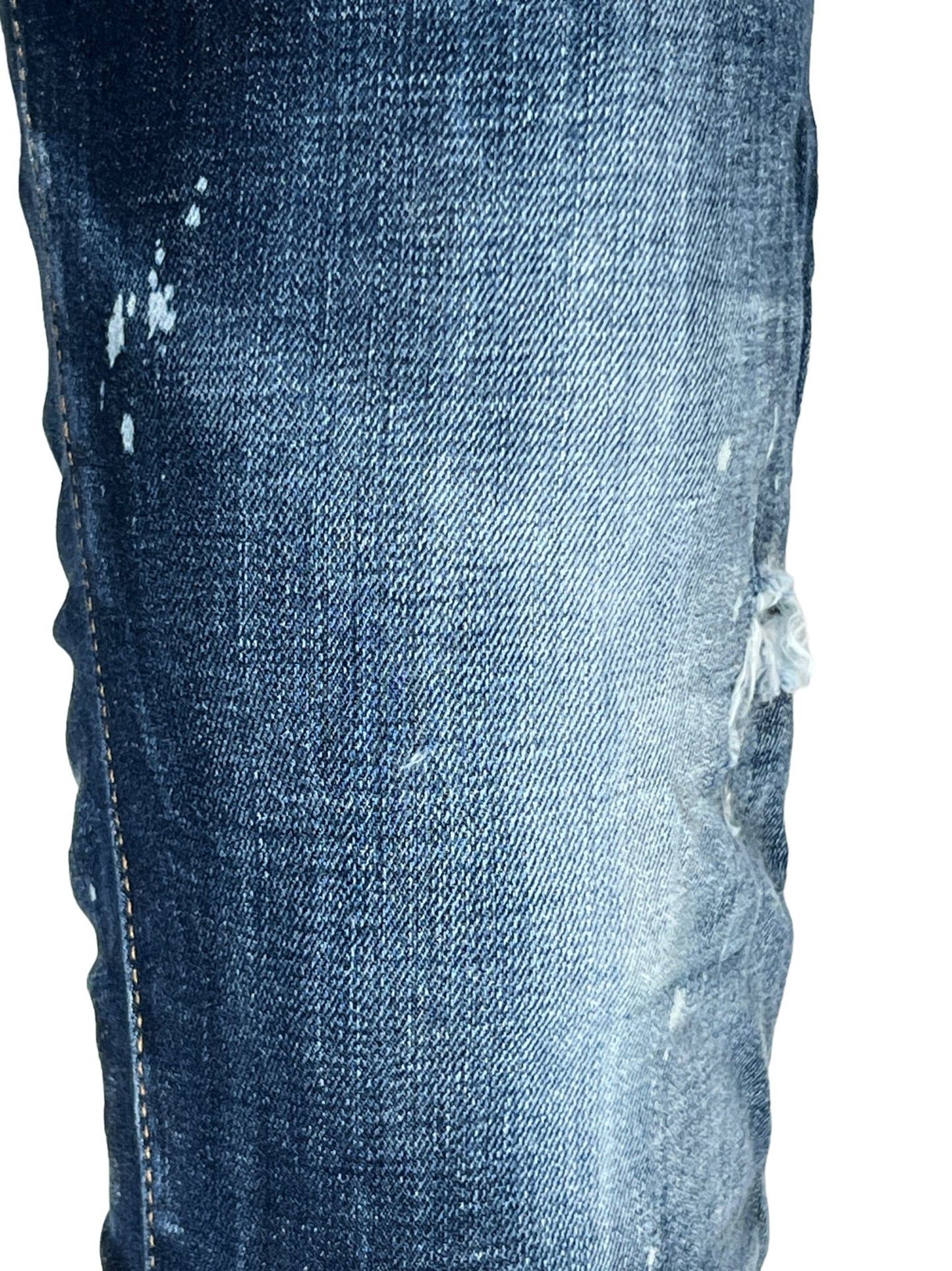 Close-up of worn DSQUARED2 S74LB1556 Skater Jeans Navy Blue with visible white paint splatters and a small tear on the right thigh, showcasing trendy ripped detailing.