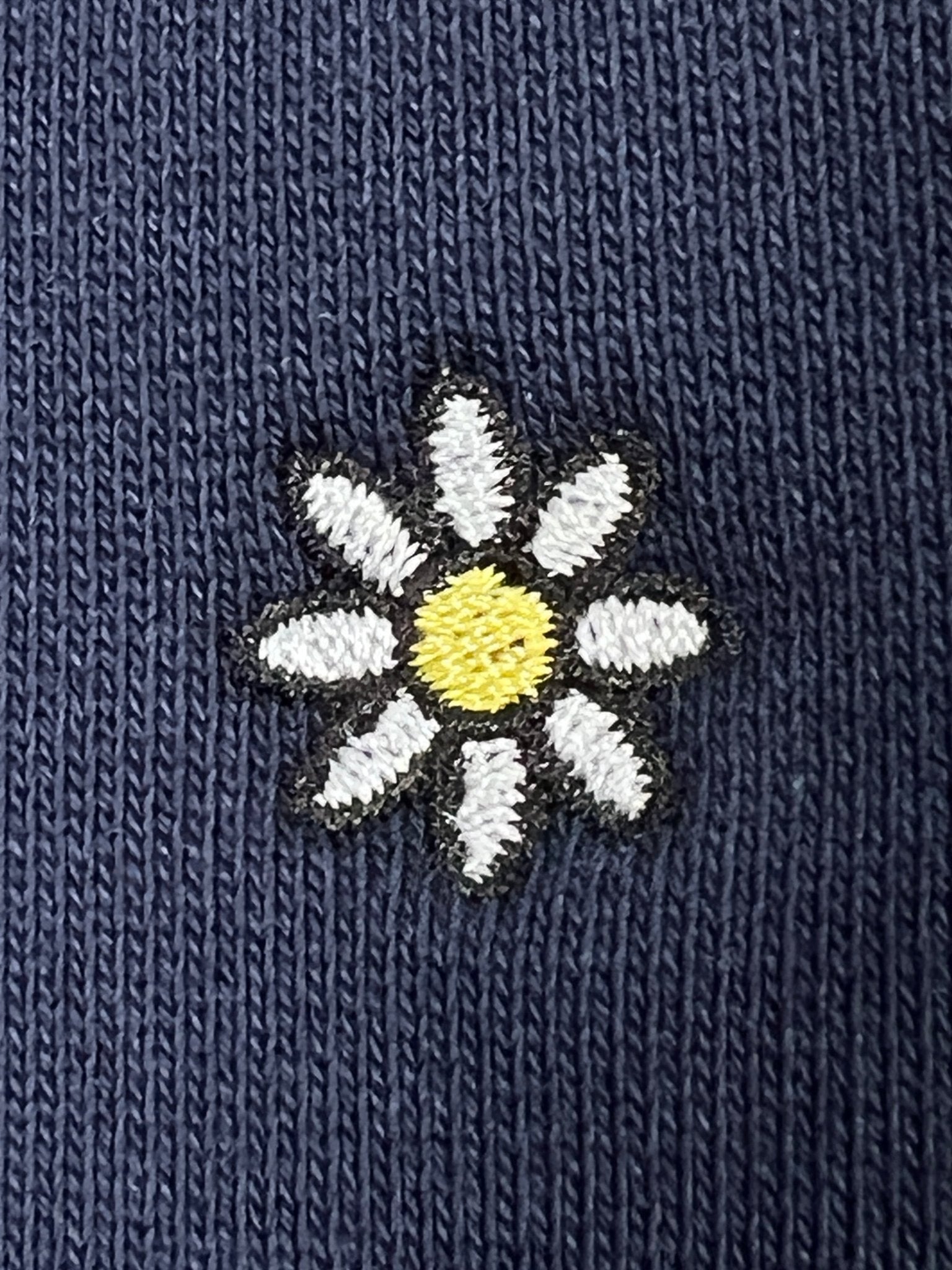 The Family First SS2502 Sweat Flower Dark Blue sweatshirt by FAMILY FIRST features an intricately embroidered white daisy with a yellow center on a dark blue fabric background, highlighting beautiful floral embroidery.