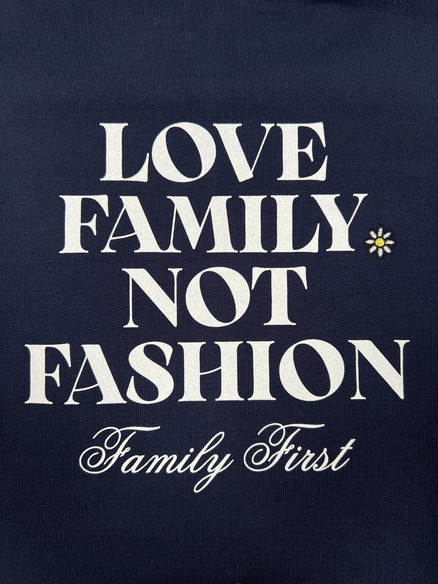 A cozy sweatshirt, Family First SS2502 Sweat Flower Dark Blue by FAMILY FIRST, features the words "LOVE FAMILY NOT FASHION Family First" with a daisy graphic on a dark background.