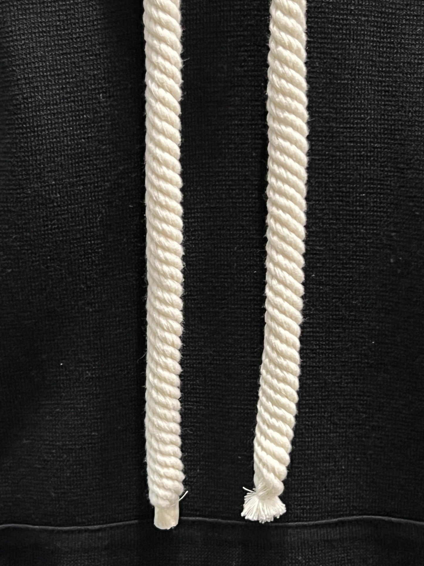 Two white rope tassels hanging vertically against a FAMILY FIRST SWS2401 HOODIE SWEATER BK fabric background with an embroidered heart logo.