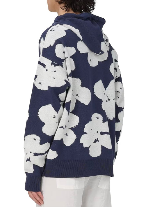Rear view of a person wearing a navy blue and white floral patterned FAMILY FIRST SWS2405 HOODIE JAQUARD DB with a hood, paired with white pants.