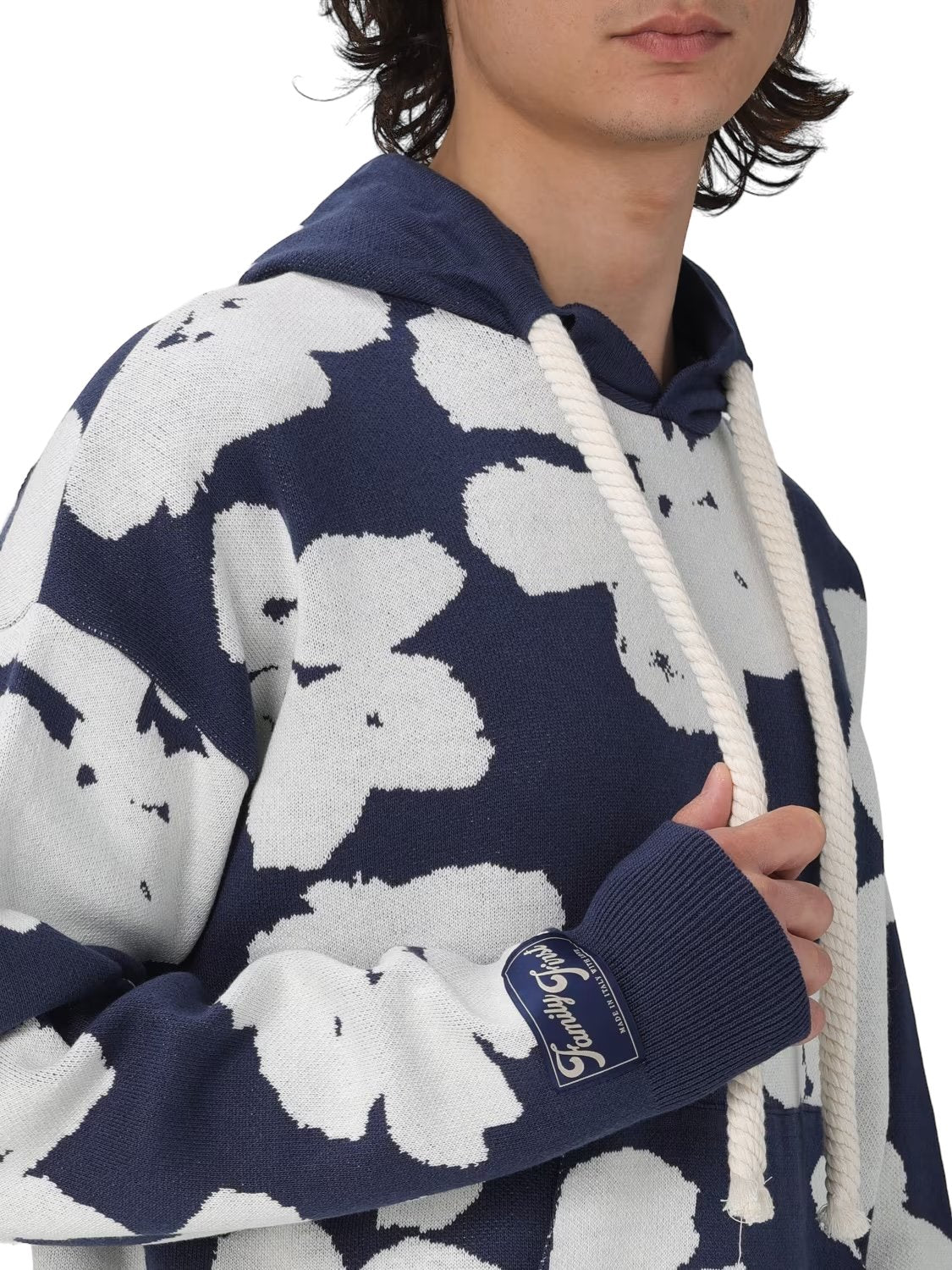 A young man wearing a navy blue and white floral patterned FAMILY FIRST SWS2405 HOODIE JAQUARD DB with a drawstring, against a black background.
