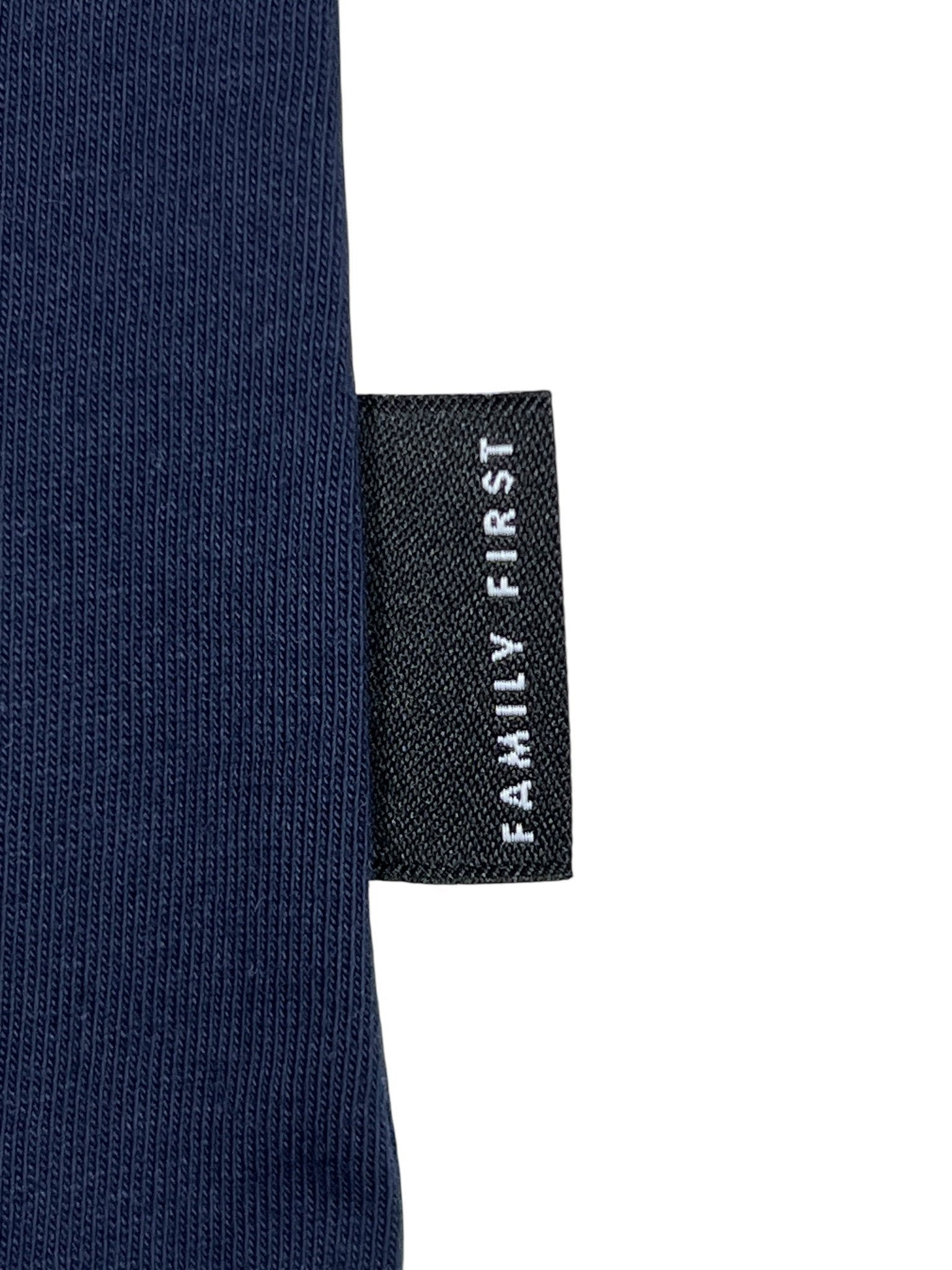 A close-up of a black fabric tag with "FAMILY FIRST" in white text complements the textured dark blue fabric of the Family First T2502DB T-shirt Flower.