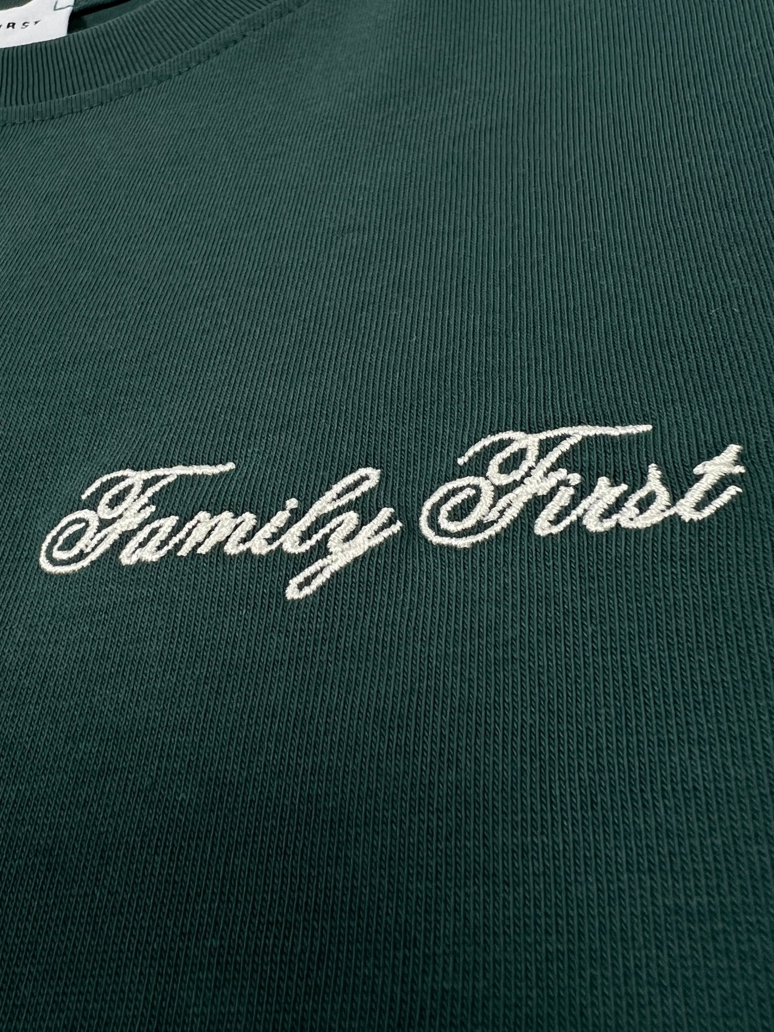 The Family First TF2409GR T-shirt in green features luxurious fabric adorned with "Family First," elegantly embroidered in white cursive lettering.