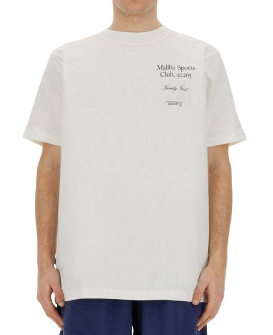 A man wearing a white graphic t-shirt with the logo "FAMILY FIRST TS2405 T-SHIRT MALIBU WHT" printed in black on the chest.
