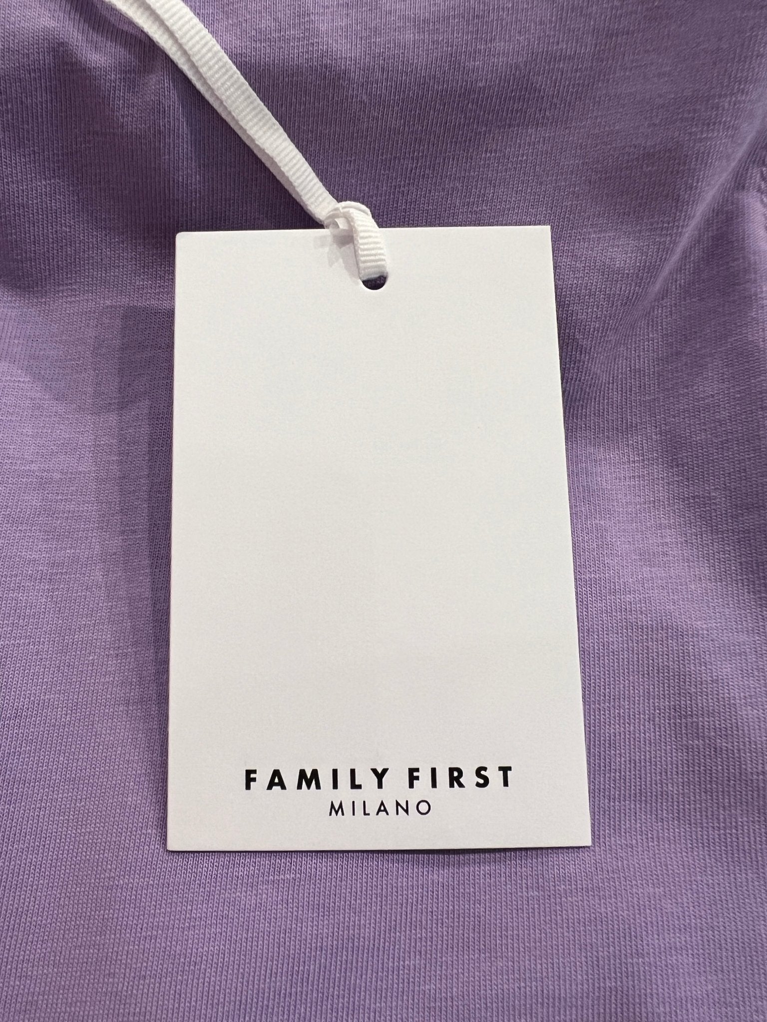 A white rectangular clothing tag with "FAMILY FIRST" is attached to the Family First TS2407 T-Shirt Swan Violet, characterized by its Italian elegance and digital print.