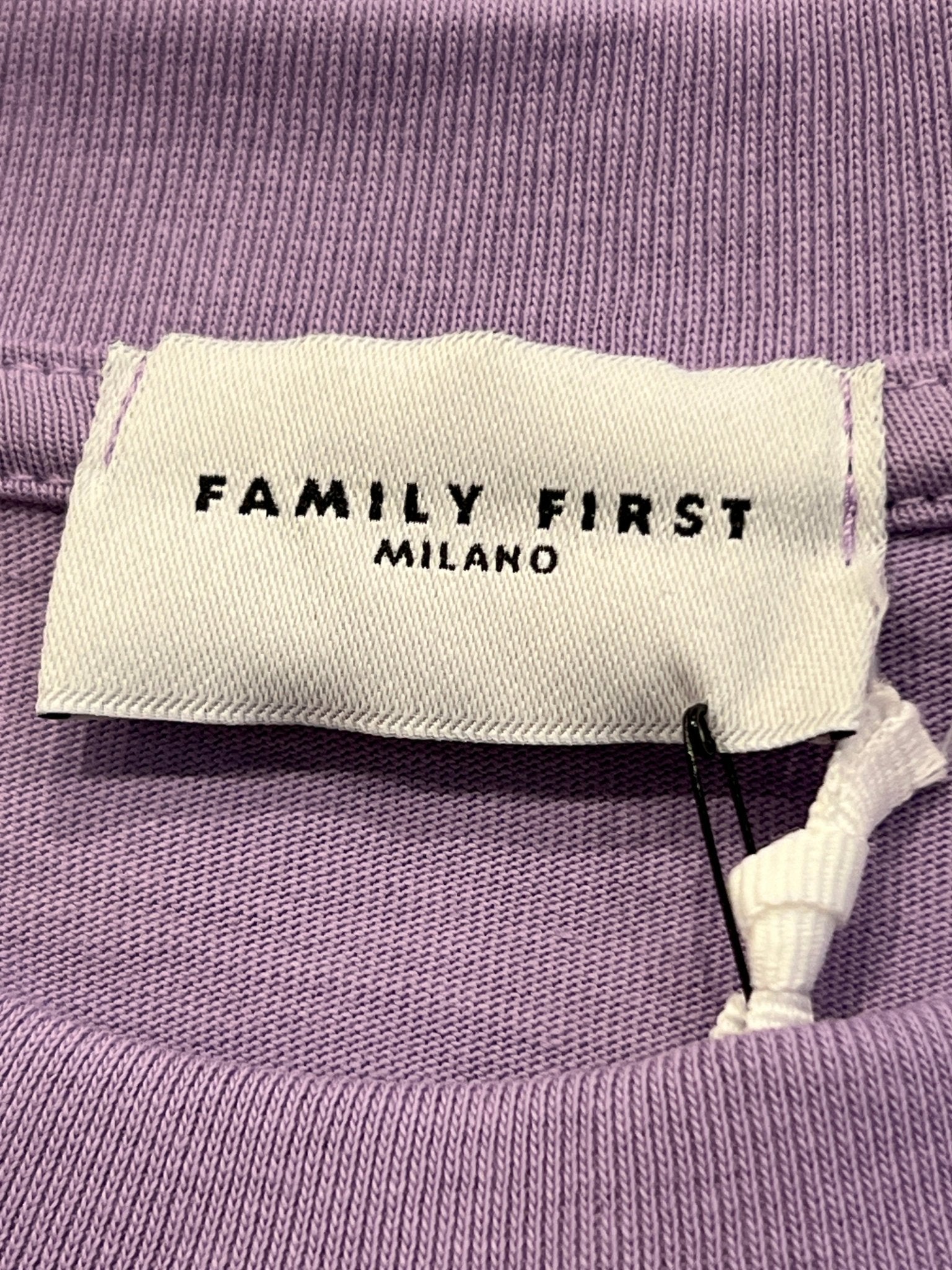 A white clothing tag with "FAMILY FIRST" in black text is sewn onto the violet fabric of the Family First TS2407 T-Shirt, capturing a sense of Italian elegance.
